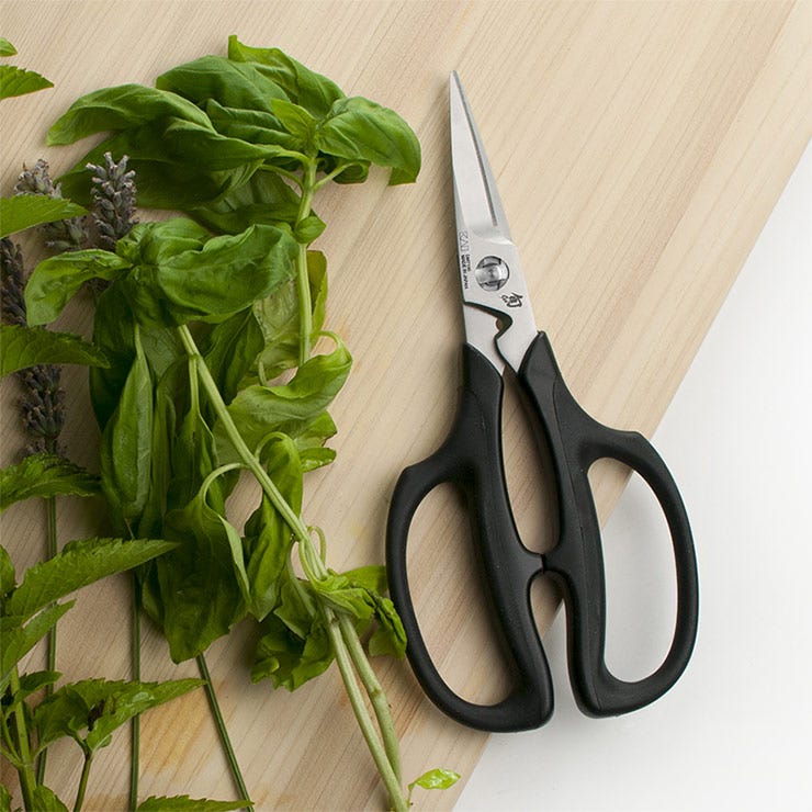 A pair of Shun Herb Shears lies next to a pile of basil leaves.