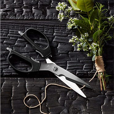 A pair of Shun Multi–purpose Shears slice through twine which is wrapped around a bundle of herbs.