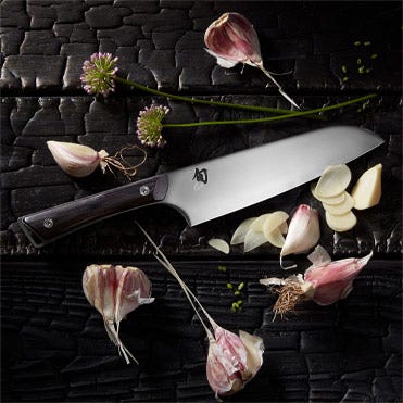 A Kazahana Santoku lies on a bed of garlic cloves.