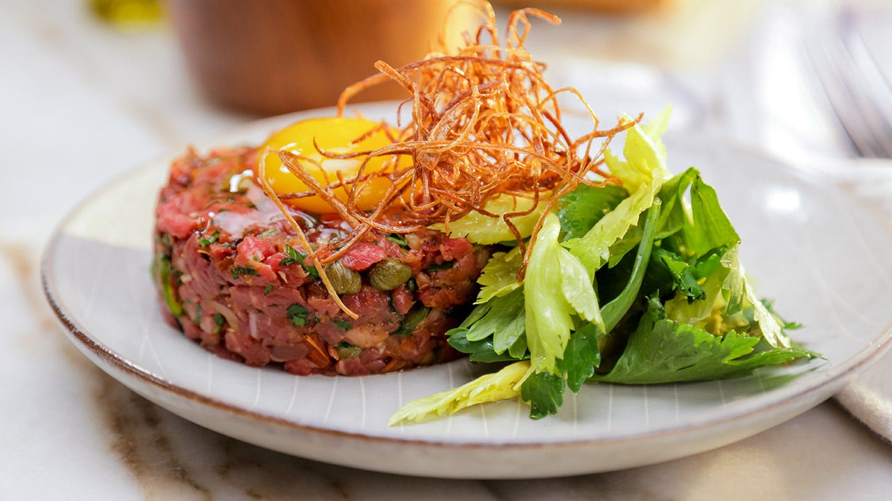 Beef Tartare on a plate with greens and a raw egg on top