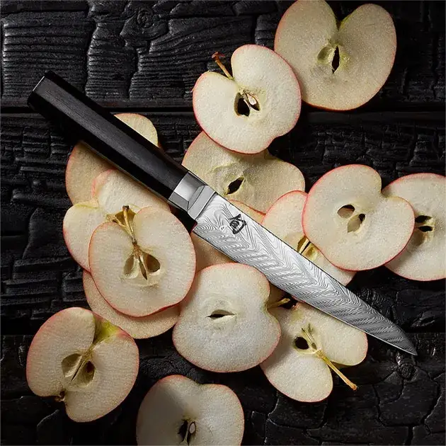 A Dual Core Utility/Butcher knife lices on thin slices of apple spread across a table.