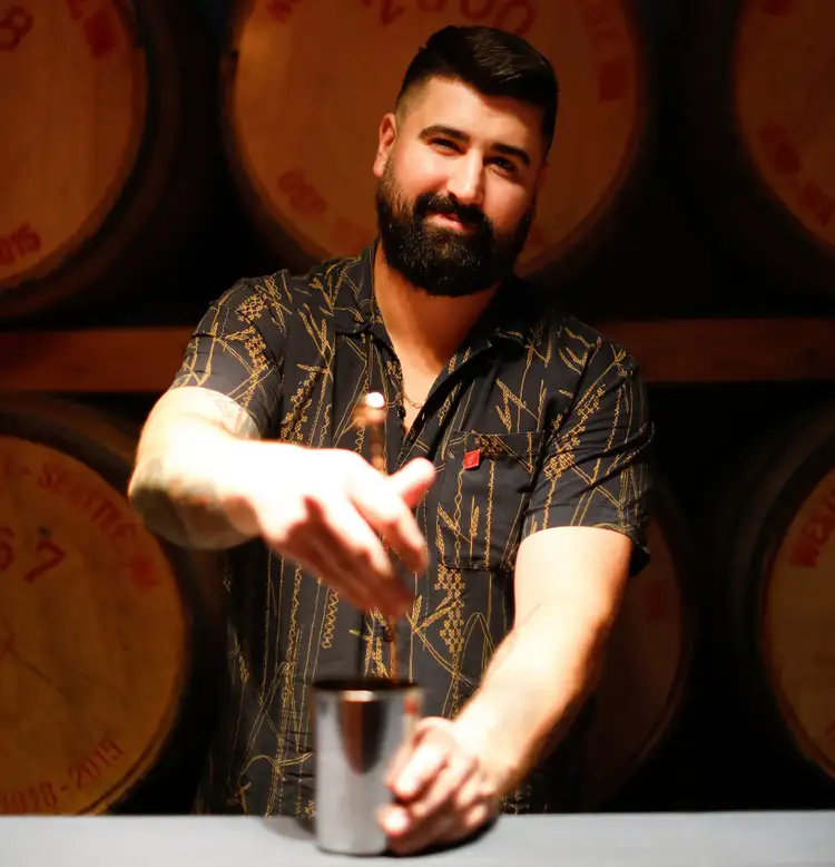 Bartender Kyton Blair mixes a drink while he smiles at the camera.