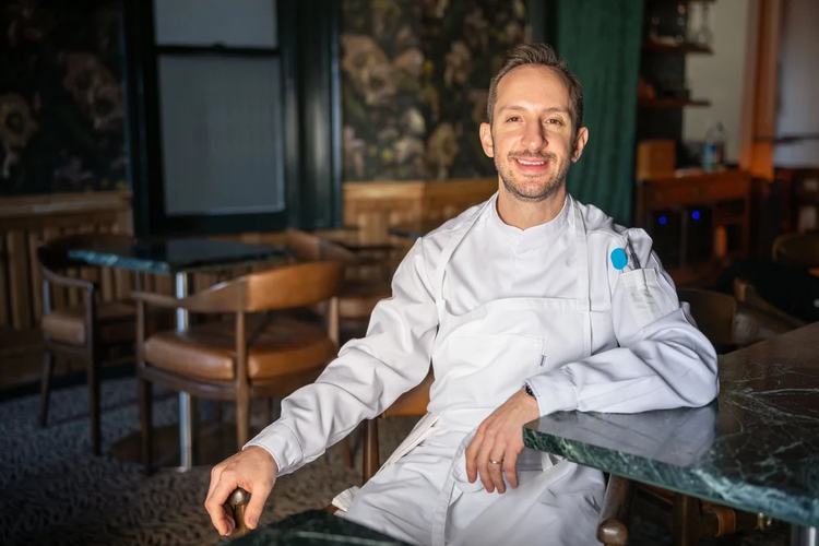 Chef Jason Chavenson sitting down in restaurant Maison Bar à Vins smiling at the camera.