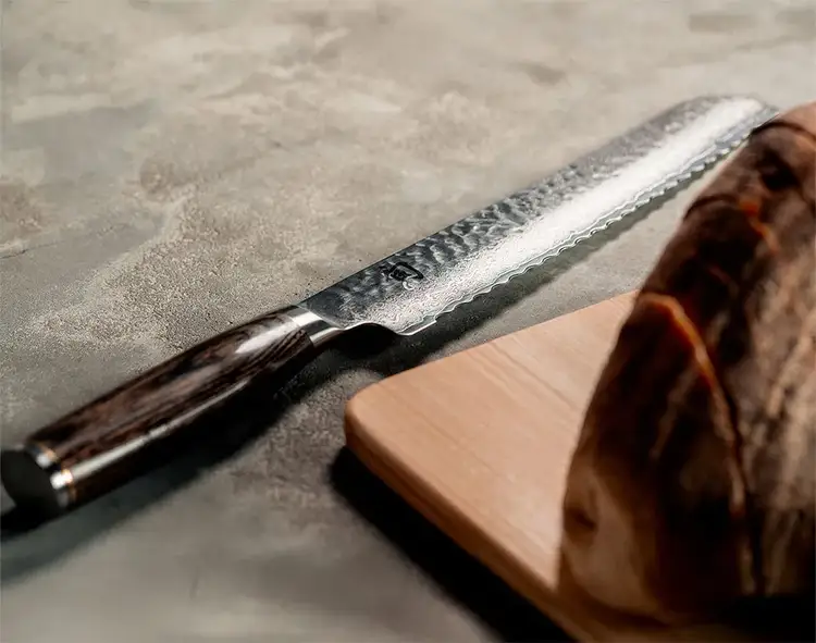 A Premier Bread Knife lays across a concrete counter next to a loaf of bed.